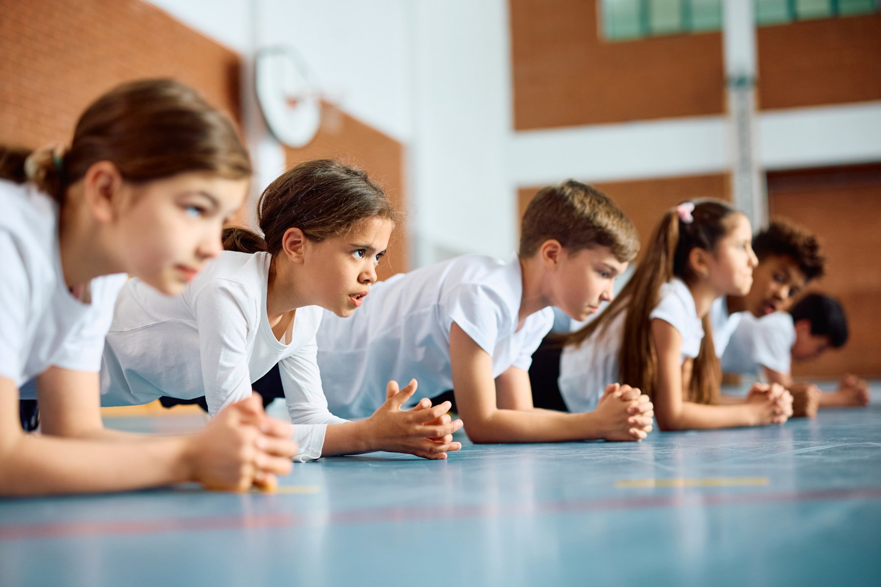 Group of schoolkids exercising during PE class at school gym.